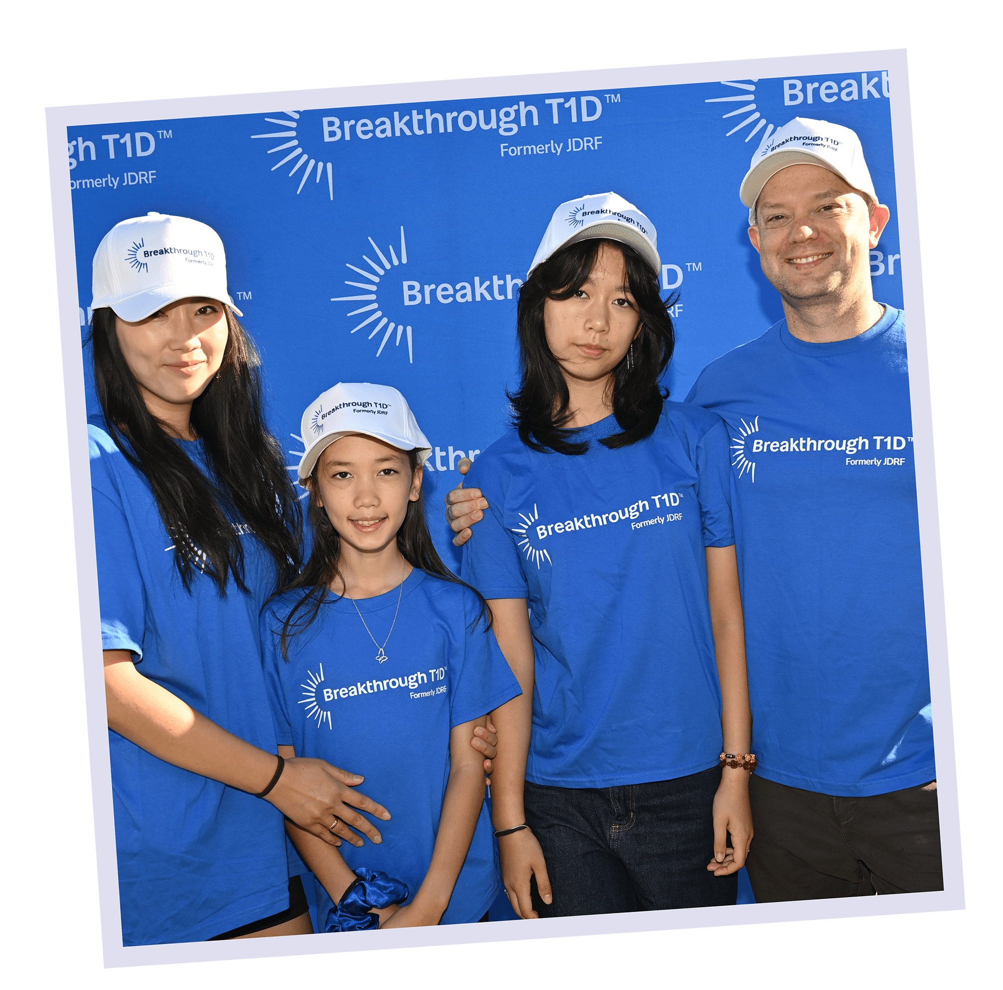 A family with 2 girls in Breakthrough T1D branded blue T-shirts smile together at an event.